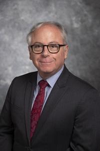 Dedman College Dean, Thomas DiPiero, smiles for a headshot in front of a gray background.