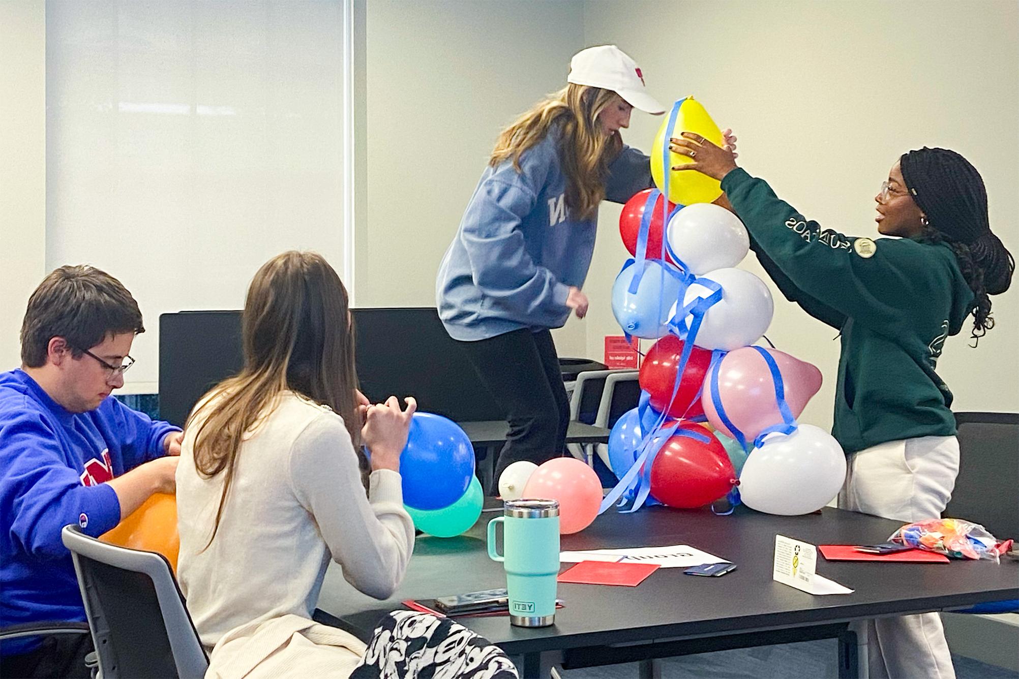 two students building tower with balloons and two students sitting at table inflating balloons